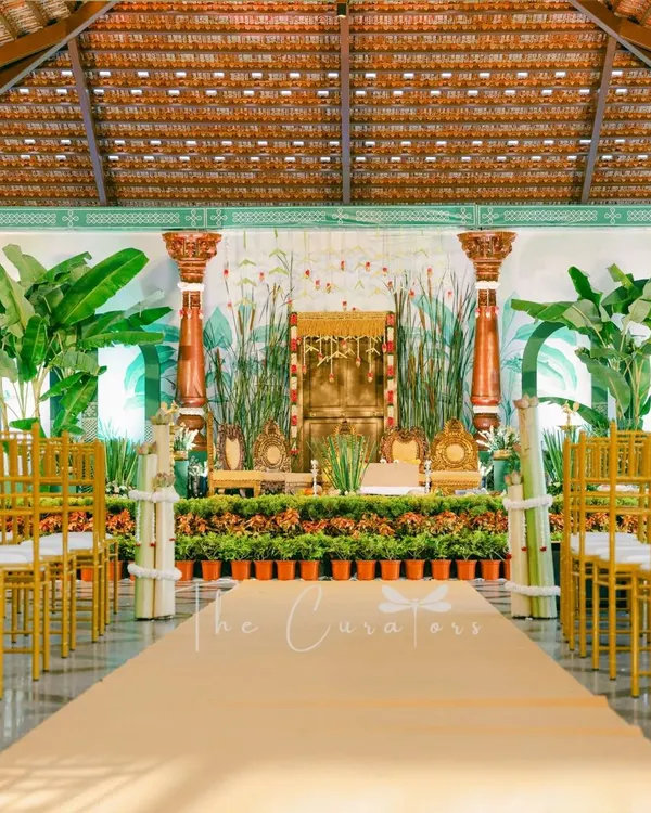 A full view of our modern Muhurtham setup, where we replaced a traditional mandap with a lush, open-air concept. The design uses rows of potted plants, banana trees, and elegant pillars to create a fresh and sophisticated atmosphere.
