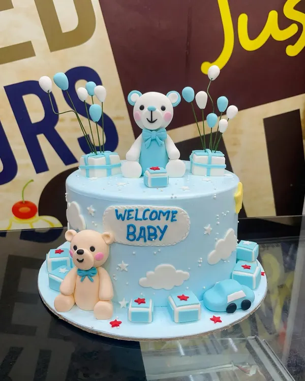 A sweet 2kg "Welcome Baby" cake in blue, adorned with cute fondant teddy bears, presents, and balloons.