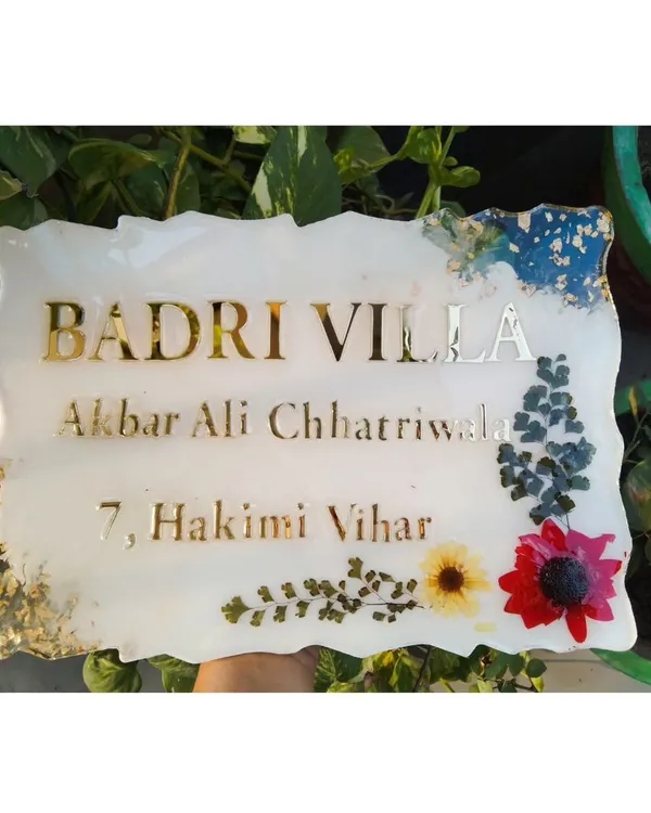 Here is the finished custom resin nameplate for "Badri Villa," shown against a natural green background. The preserved flowers and gold details stand out beautifully.