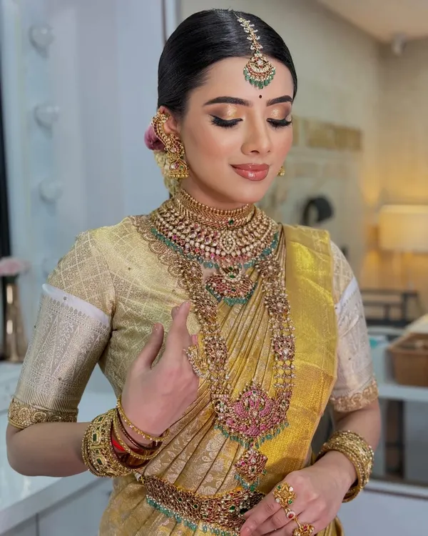 A breathtaking Muhurtham look in a golden Kanjeevaram saree. The makeup features a warm, glowing complexion, classic gold eyeshadow, and a perfectly defined lip, complemented by heavy temple jewelry for a regal finish.