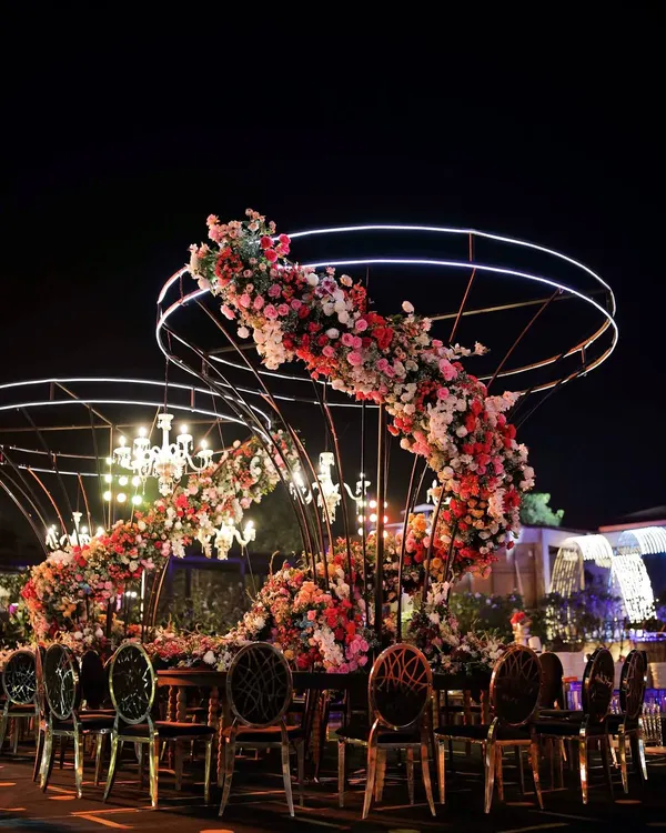 A breathtaking floral spiral centerpiece designed for a Sangeet night, where modern structure meets classic romance. This custom installation, illuminated by elegant chandeliers, creates an intimate yet grand dining experience under the stars.