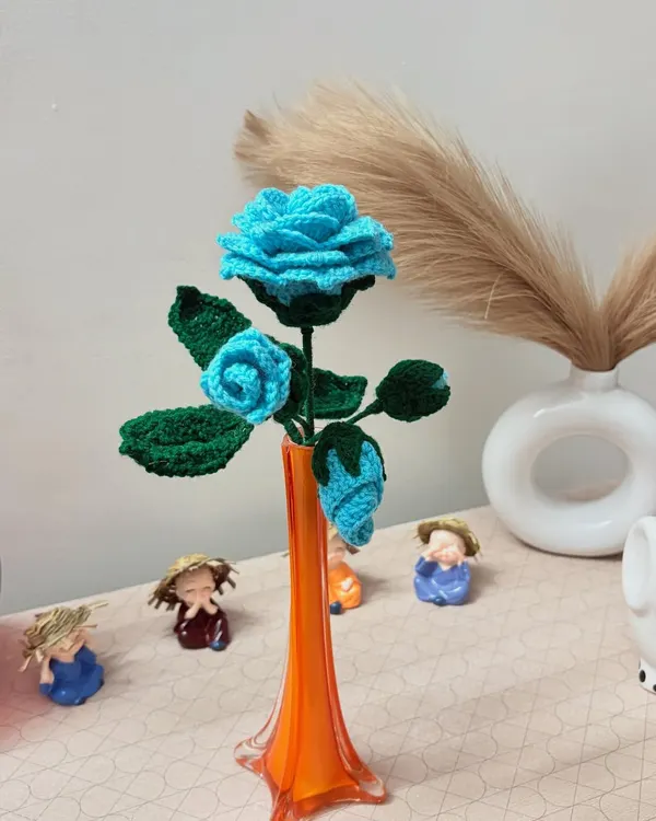 A handcrafted crochet blue rose stem with multiple flowers and buds, placed in a vase to show how it can enhance your home decor.