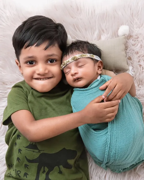 A proud big brother gives his newborn sibling a happy, toothy grin and a gentle hug. This shot perfectly captures the joy and excitement of a growing family.