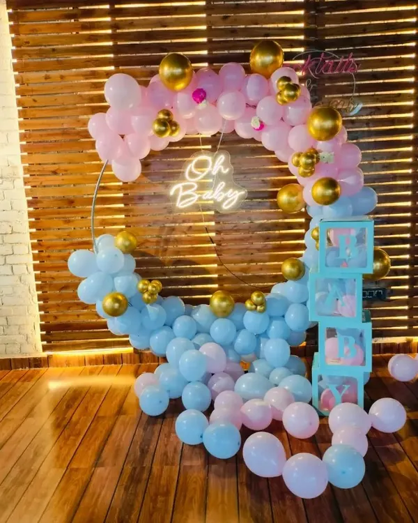 A beautiful "Oh Baby" setup perfect for a gender-neutral baby shower or a gender reveal party. The circular balloon arch uses a soft pink and blue palette with gold accents, complemented by "BABY" blocks and a warm neon sign.