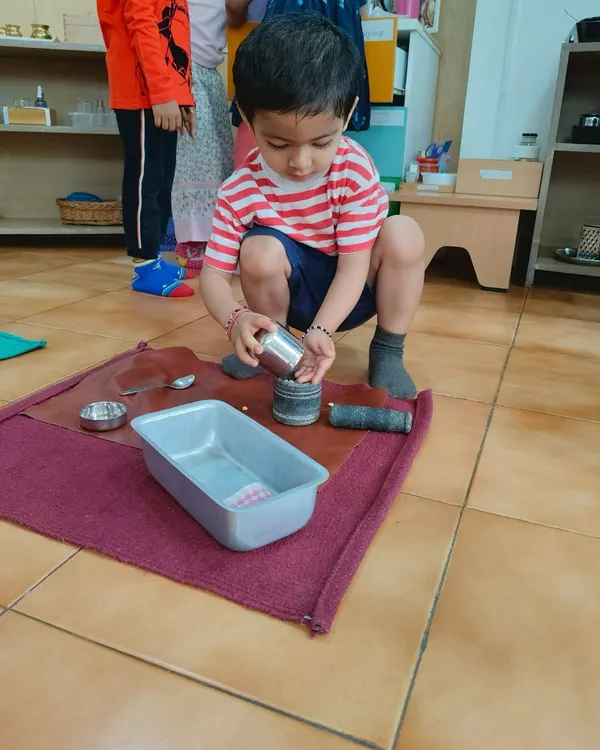 A child carefully pouring from one container to another. This simple activity is a lesson in precision, control, and concentration, building skills that are essential for writing and other academic work.