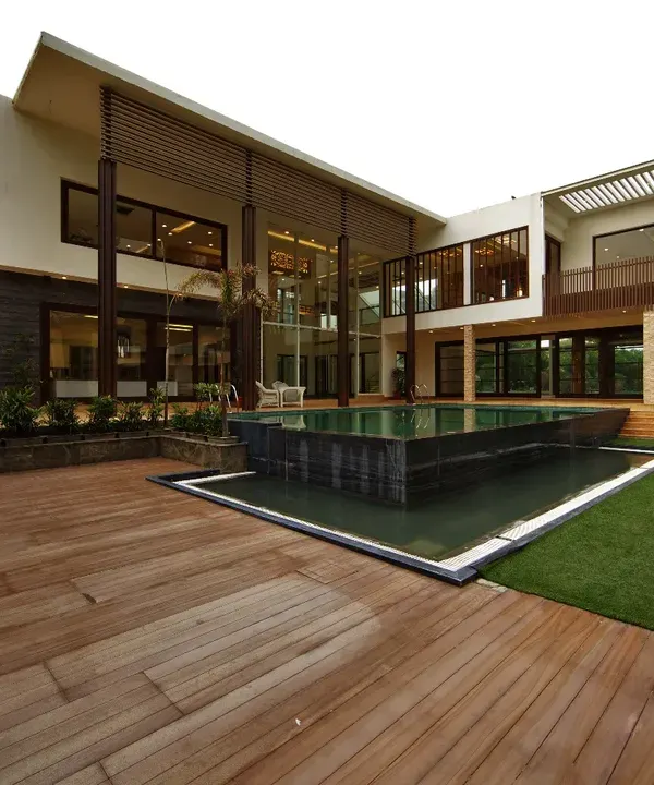 The Sachdeva Farmhouse is designed with the pool as its heart. The architecture wraps around this central courtyard, with a wooden deck and green lawn creating a seamless transition between the built form and the landscape.