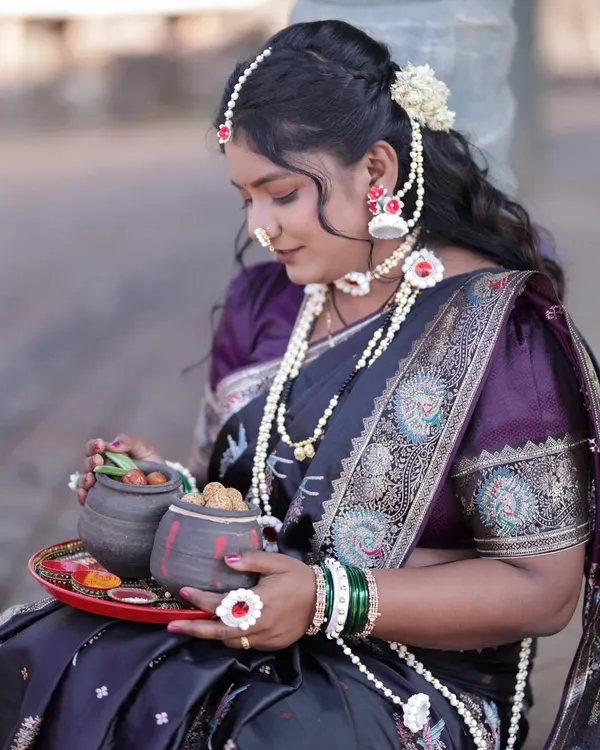 The complete Makar Sankranti look, featuring a black saree with a peacock border, a purple blouse, and the special halwyache dagine.
