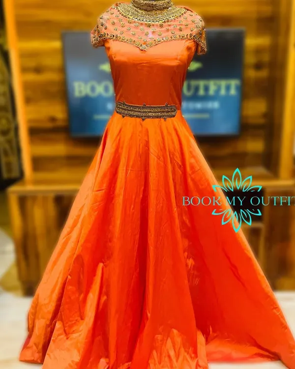 Make a bold statement in this vibrant orange ball gown. The intricate, high-neck beadwork and belted waist create a regal silhouette, making it an ideal rental for sangeets, weddings, or formal gatherings.