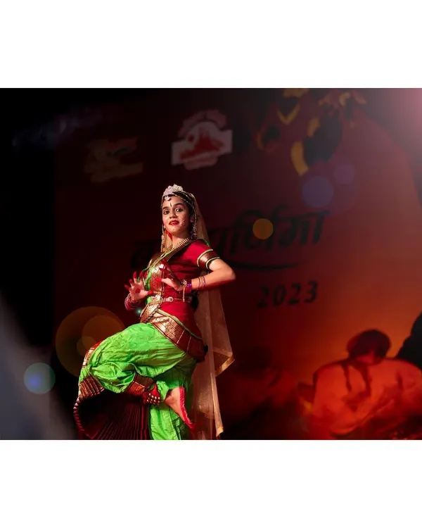 A Bharatanatyam dancer is captured mid-performance on stage, with a dramatic lens flare adding to the energy. My technical setup with a Nikon Z6 and Godox lighting ensures crisp images even in challenging, fast-paced stage environments.