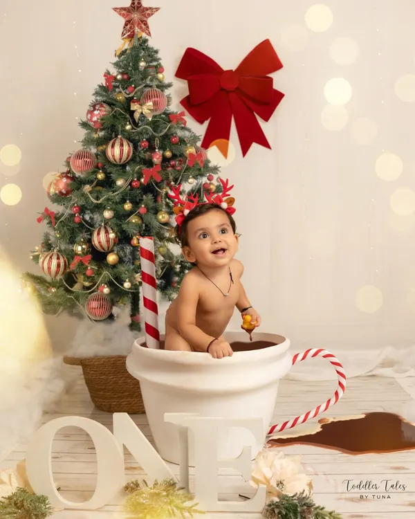 A one-year-old enjoys a creative "hot chocolate" bath session against a festive Christmas backdrop. This shows a glimpse into my fun, themed milestone shoots.