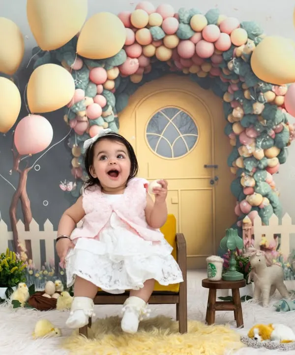 We believe a first birthday is a fairytale moment. This magical hobbit-door setup, complete with a pastel balloon arch, is just one example of how we create enchanting worlds for your child's milestone photoshoot.
