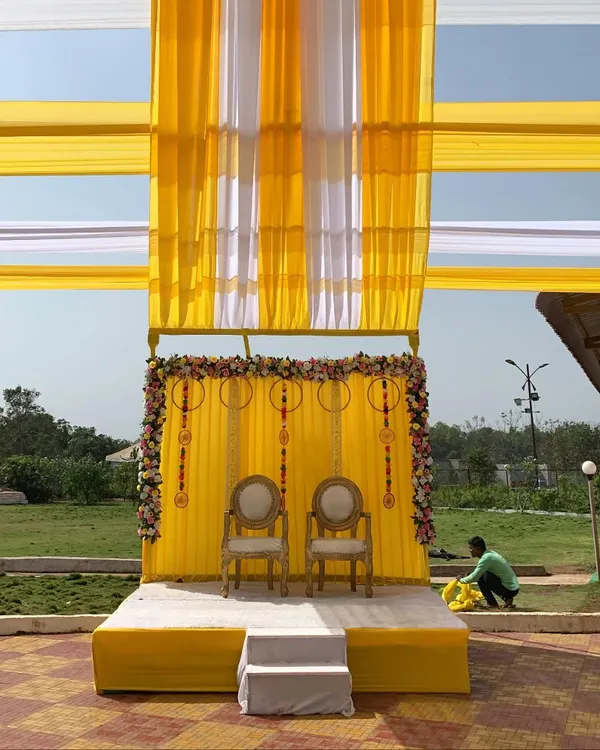 A classic outdoor Haldi stage setup. I used bright yellow and white drapes for the canopy, with a floral-framed yellow backdrop and traditional chairs for the ceremony.