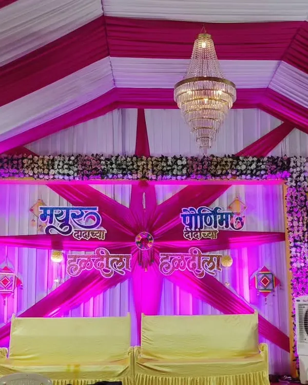 A fun and vibrant Haldi stage, perfect for a lively celebration. The decor uses bright pink and white drapes, personalized name boards for 'Mayur' and 'Purnima', and traditional elements to create a festive atmosphere.