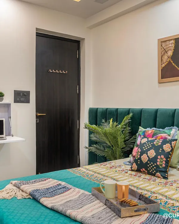This beautiful emerald green bedroom was designed with functionality in mind. It features a fold-down study desk, perfect for small spaces, and a comfortable bed with vibrant, patterned cushions.