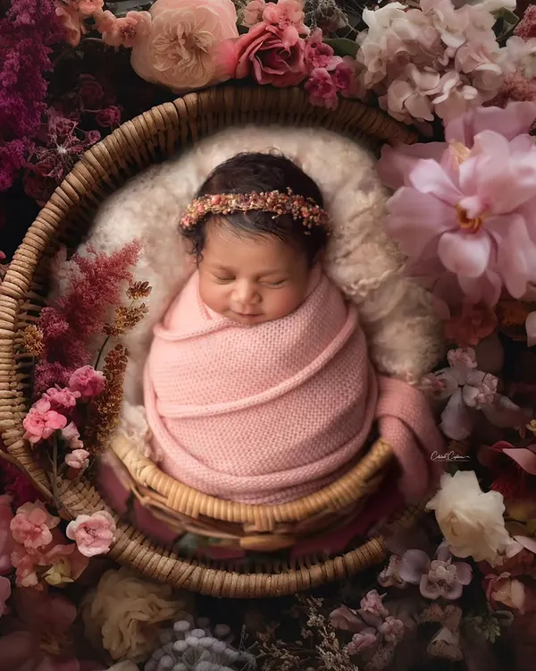 A breathtaking portrait of a baby girl nestled in a basket overflowing with a rich tapestry of flowers. This is a perfect example of a lush, fine art botanical setup.