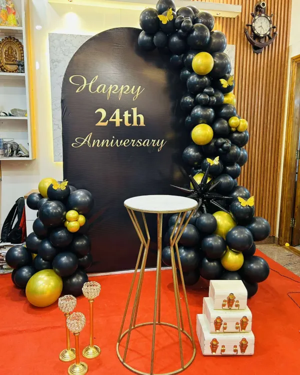 I also provide decorations for anniversaries, like this elegant setup for a 24th anniversary. The black backdrop with gold lettering is framed by a black and gold balloon arch, creating a sophisticated and celebratory look.