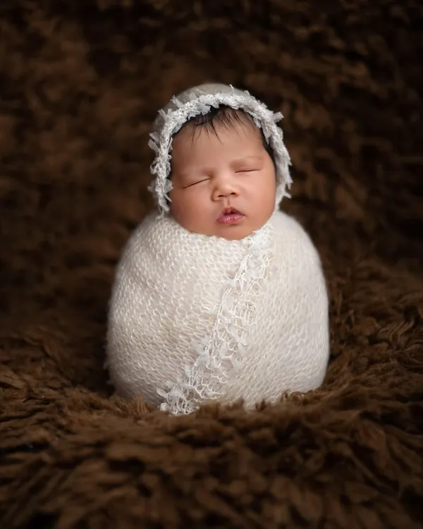 Perfectly swaddled and sleeping soundly. This classic newborn portrait, known as the potato sack pose, highlights the baby's peaceful features while ensuring they are snug, safe, and comfortable.