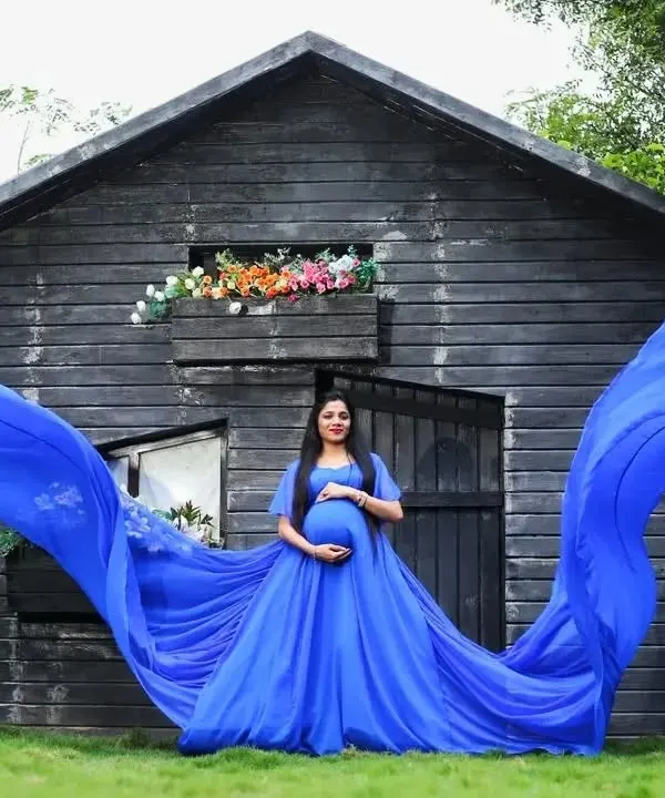 A vibrant royal blue gown with a long, flying trail creates a breathtaking image against a rustic outdoor backdrop. This is a perfect example of a high-impact outdoor maternity portrait.