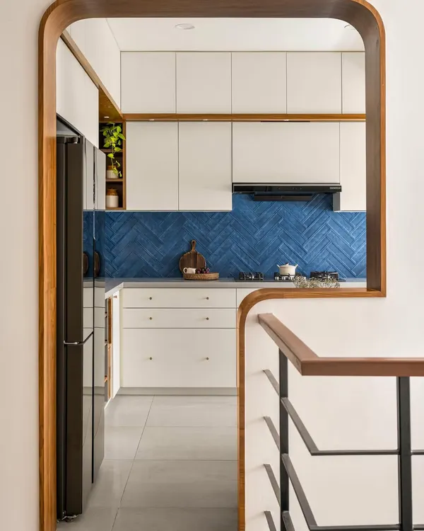 In our 'Palaash' project, we used a bold blue herringbone tile backsplash to create a stunning focal point. The kitchen is viewed through a custom wood-framed arch, connecting it beautifully to the rest of the home.