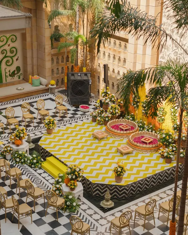 An aerial view of a vibrant Haldi setup in an inner courtyard, featuring a modern yellow and white chevron stage floor. This shows how I blend contemporary patterns with traditional ceremony spaces.