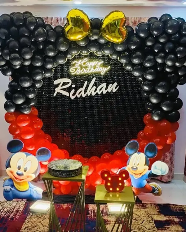 A classic Mickey Mouse themed birthday setup with a black sequin backdrop and a balloon arch shaped like Mickey ears.