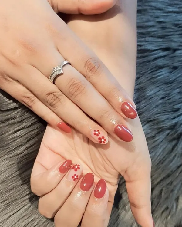 A simple and sweet design with a reddish-brown polish and a delicate red floral pattern on the accent nails.