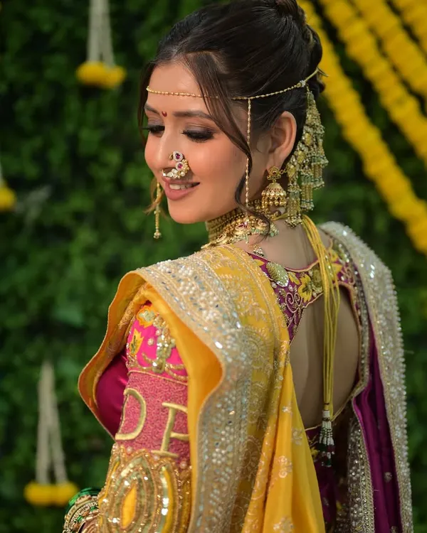 A truly authentic Maharashtrian engagement look. The makeup is soft and radiant, with attention to the eyes and the traditional mundavalya and earchain. The yellow and pink saree combination is vibrant and celebratory.