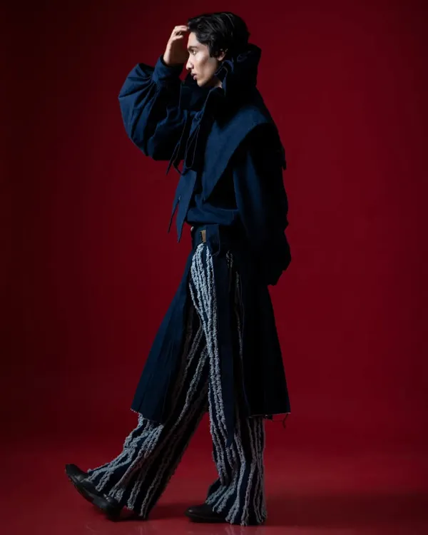 A high-contrast fashion story. The clash of the bold red background with the deep blue, avant-garde outfit creates a visually arresting image.