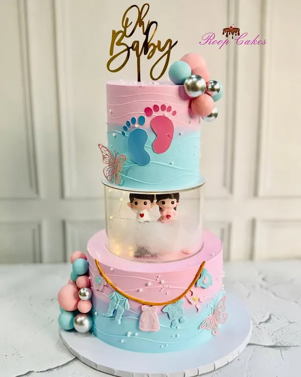 Sweet beginnings and a little bundle of joy on the way. This grand three-tier baby shower cake features pink and blue ombre, tiny fondant clothes, and cute baby figurines peeking out from the middle tier.