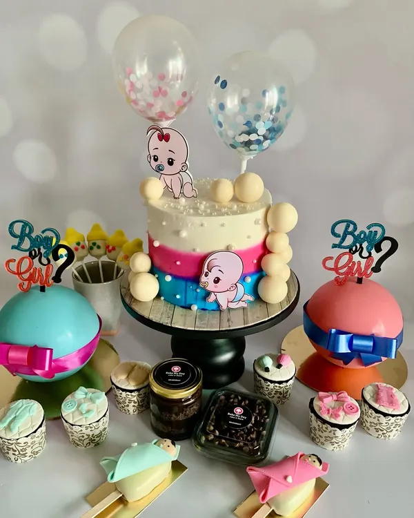 A complete gender reveal dessert table featuring a custom cake with balloon toppers, themed breakable chocolate domes, adorable cakesicles, and assorted treat jars. This is how I turn a party into a full-blown celebration.