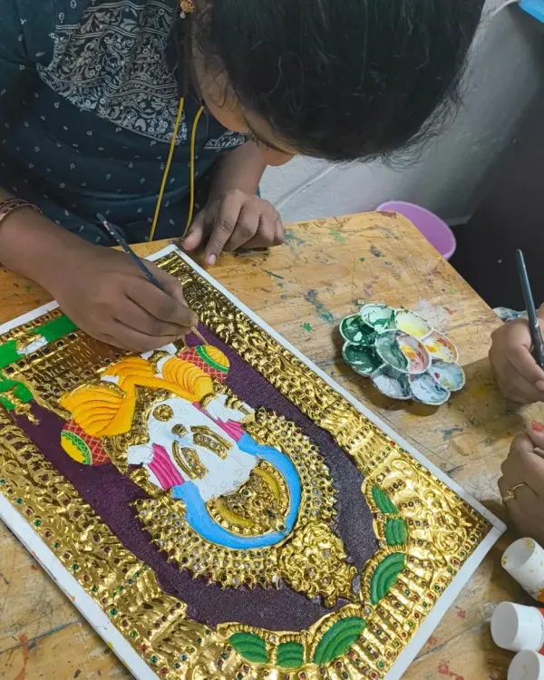 A student carefully applies gold leaf to a Tanjore painting. This traditional art form requires immense patience and precision, skills that are valuable for any aspiring artist.