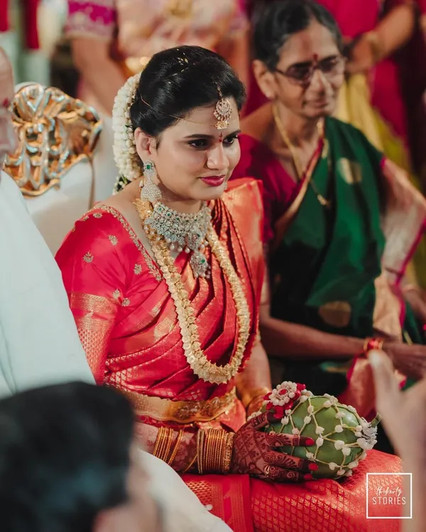 A candid portrait of a bride in a stunning red saree during her wedding ceremony, her expression full of gentle emotion.
