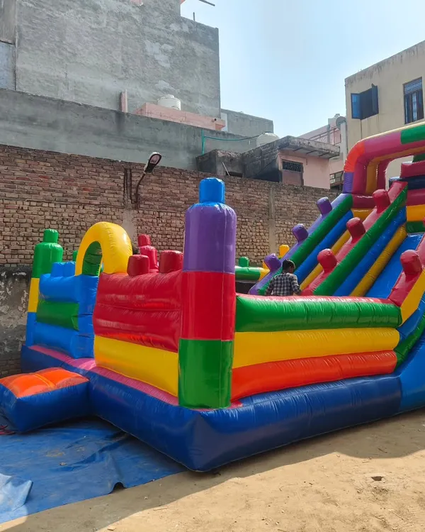 A new model of a large, colorful bouncy castle with multiple activity zones. A person is standing next to it, showing the impressive scale of the structure.
