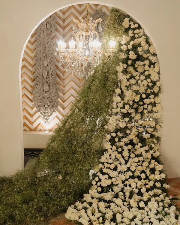 I create fairytale entrances that set the tone for the entire event. This stunning archway, overflowing with baby's breath and white roses, frames a view of a crystal chandelier, promising a night of elegance.