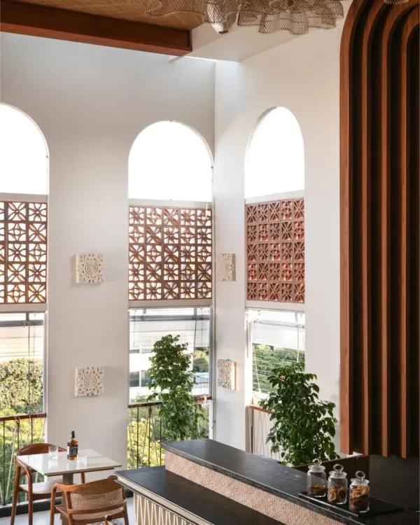 We transformed a bare concrete shell into a slice of Bali in the city. The double-height arched windows flood the space with sunlight, while handmade terracotta jalis and tropical plants bring an earthy, serene island soul to this urban cafe.