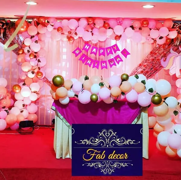 A full view of a unicorn-themed birthday stage I designed. The setup features a large balloon arrangement in pinks and golds, a decorated cake table, and unicorn character elements to bring the theme to life for a baby girl's party.