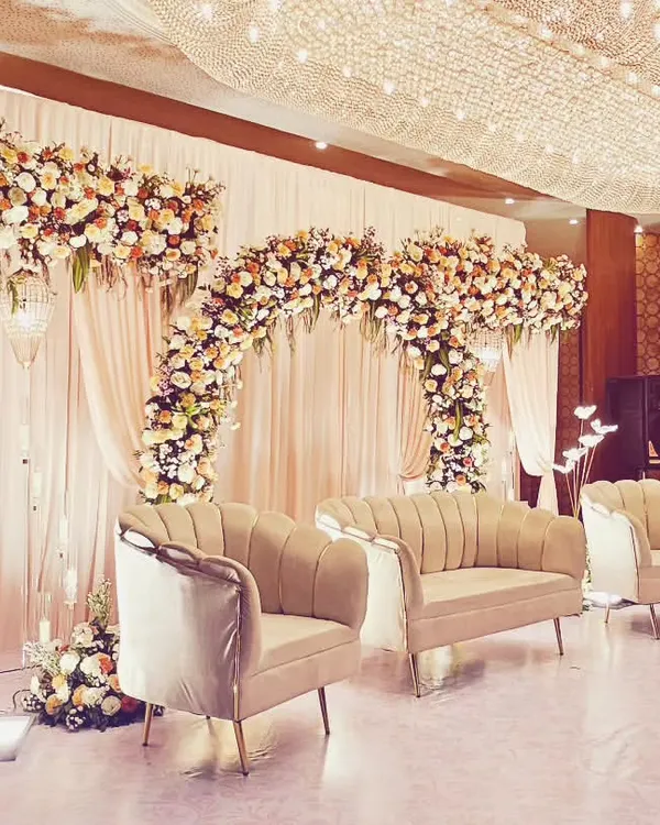 A classic and grand reception stage featuring lush floral arches in pastel shades, elegant drapery, and a magnificent crystal chandelier overhead. This timeless design exudes sophistication and romance for a perfect wedding celebration.