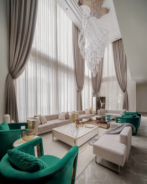 We believe a living area should not just look grand, but feel inviting. In this double-height space, we used soaring drapes and a statement chandelier to create drama, while the plush seating in neutral tones and pops of emerald green makes it a space you want to sink into. It’s the perfect example of our quiet luxury philosophy.