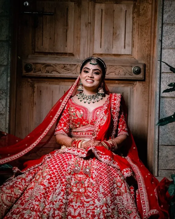A breathtaking bridal portrait. This bride looks absolutely radiant in her red lehenga, seated in a way that showcases the grandeur of her outfit.