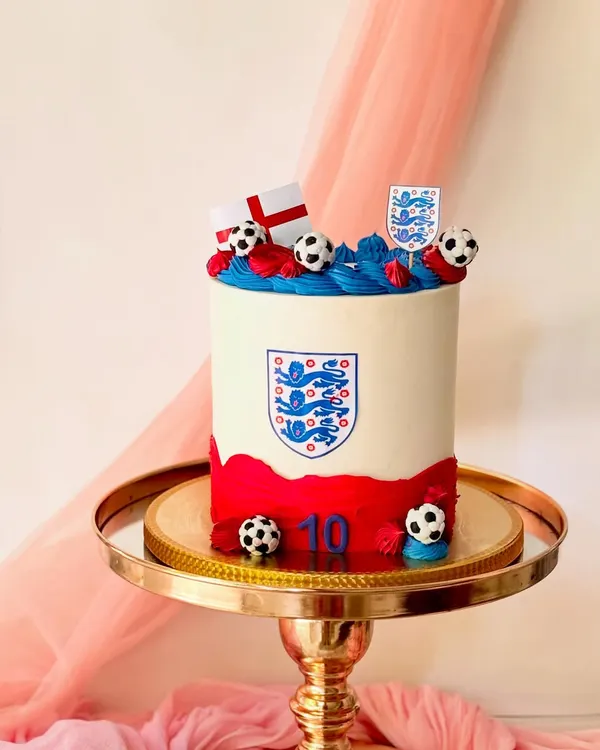 A cake for a fan of the England football team. This design features the team crest, the English flag, and fondant footballs on a clean buttercream base.
