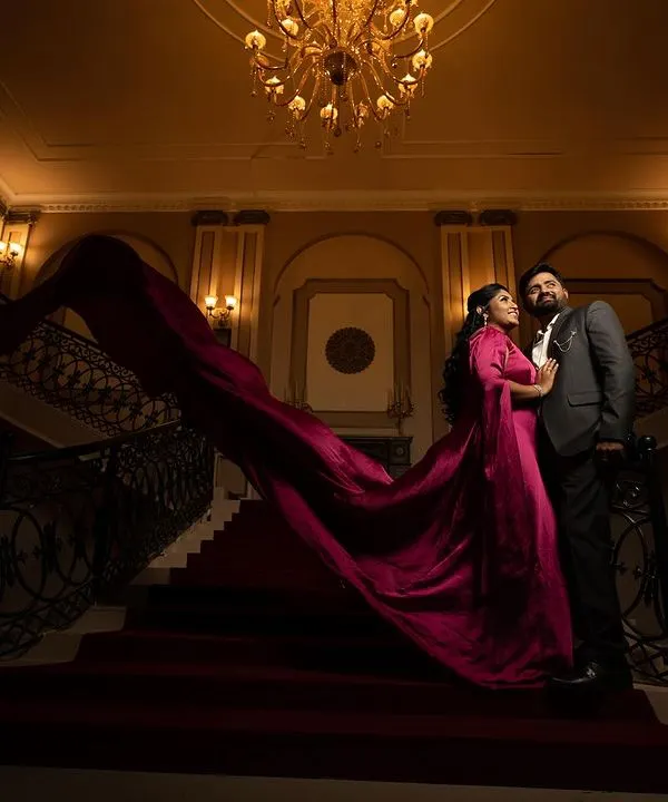 A low-angle shot emphasizing the grandeur of a palatial staircase, with the couple in formal wear and her magenta gown creating a dramatic, fairy-tale scene.