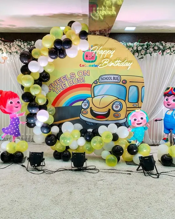 A fun Cocomelon-themed birthday party setup for a young child. I created a custom circular backdrop with characters from the show, framed by a balloon arch in a yellow, black, and white color scheme.