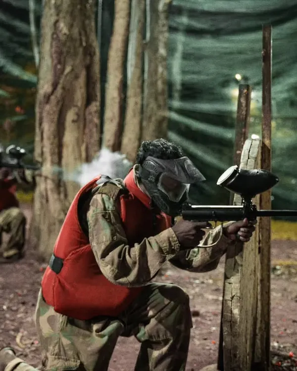 Aim. Shoot. Conquer. A player takes cover and fires during an intense paintball match in our wooded arena.