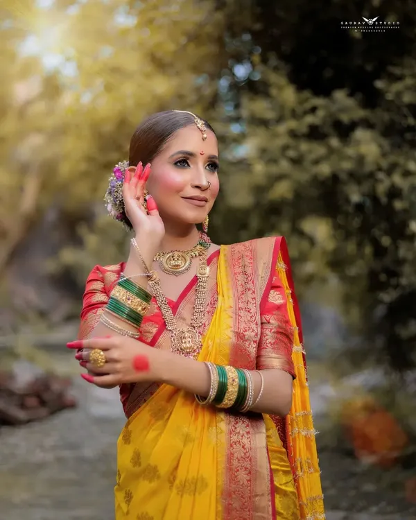 A beautiful outdoor portrait of a model in a traditional yellow Maharashtrian saree, her pose graceful and elegant.