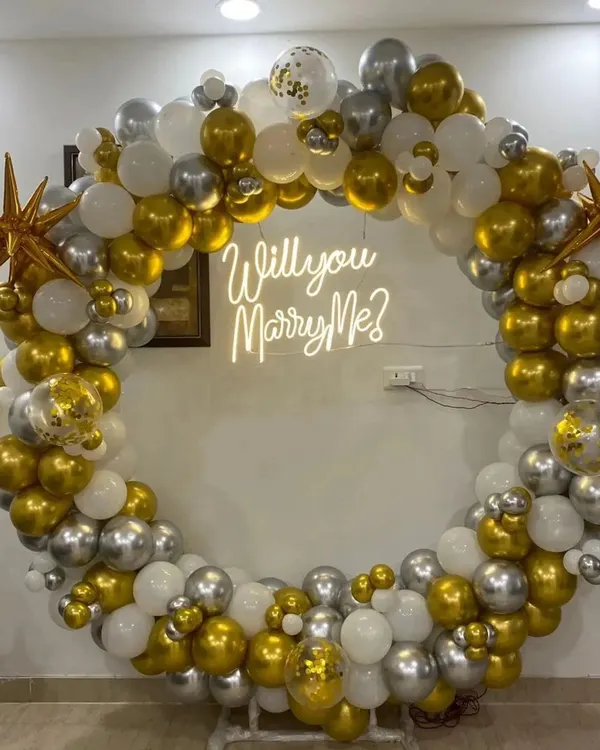 This proposal ring backdrop is one of my most popular items. The full circle of balloons in gold, silver, and white creates a stunning frame for the "Will you Marry Me?" neon sign.