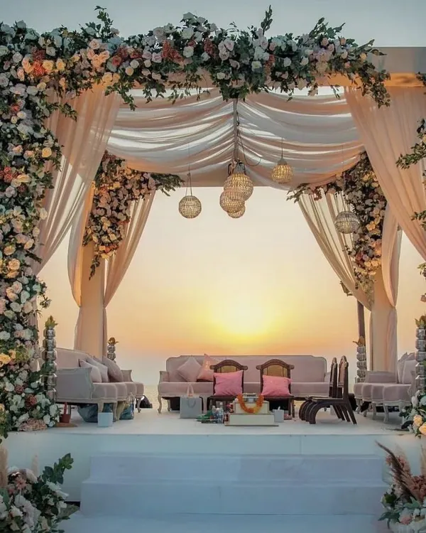 A romantic sunset mandap on a beach, with lush floral pillars and soft, flowing drapes. This setup is perfect for an intimate and picturesque destination wedding.