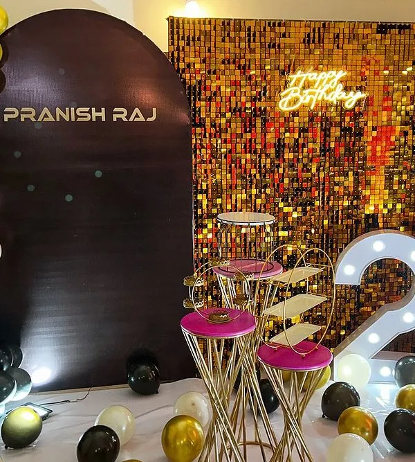 A glamorous 23rd birthday setup in black, white, and gold. This decor features a gold shimmer wall, a personalized backdrop, a neon "Happy Birthday" sign, and large light-up marquee numbers.