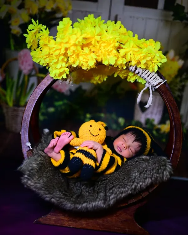 An adorable newborn photoshoot featuring our bumblebee costume. The baby is sleeping peacefully in a basket, complete with a matching toy and yellow flowers.