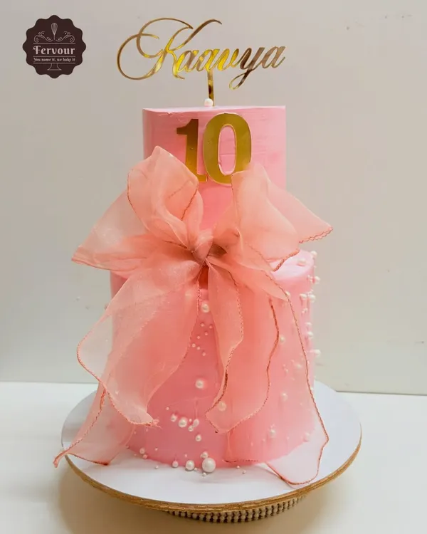 A pretty pink two-tier cake for a 10th birthday, decorated with a large, delicate organza bow. This design is simple, elegant, and very chic.