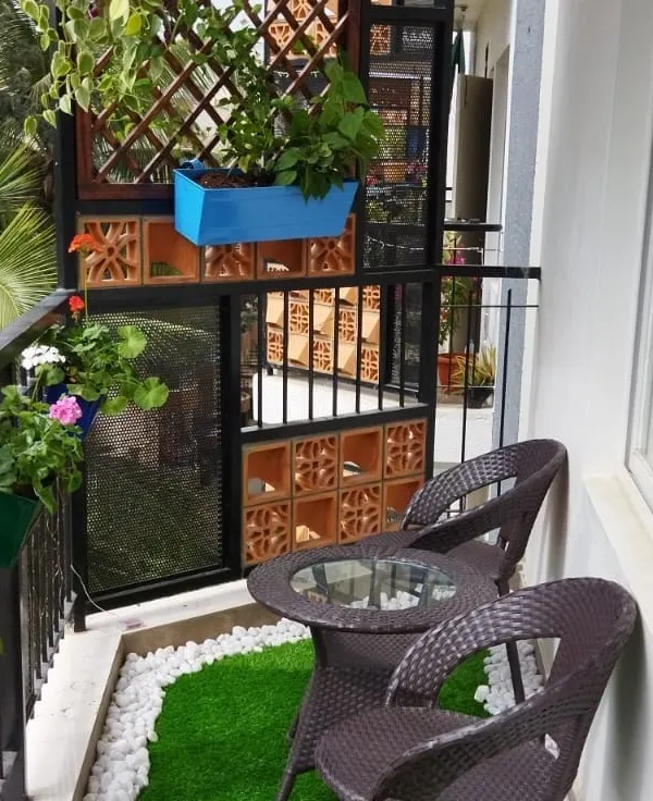 We designed this cozy balcony seating nook, complete with a small table and chairs. The space is decorated with railing planters, a wooden trellis with a climbing plant, and artificial grass with a white pebble border.
